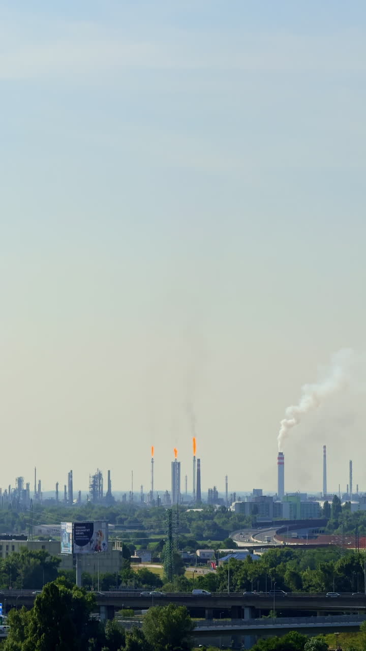 Industrial skyline with smoke and flames. Smoke billows from refinery towers as gas flares burn brightly in the skyline under a clear, blue sky