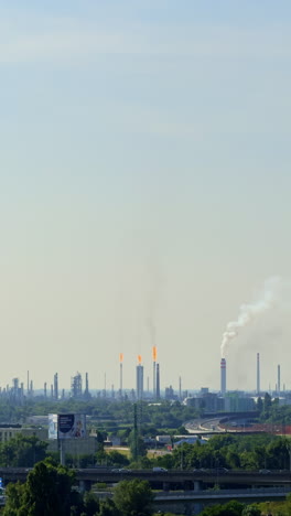 industrial skyline with smoke and flames. smoke billows from refinery towers as gas flares burn brightly in the skyline under a clear, blue sky