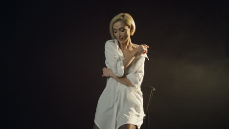 front view of caucasian young female model posing in the dark studio with smoke while the photographer taking shots of her