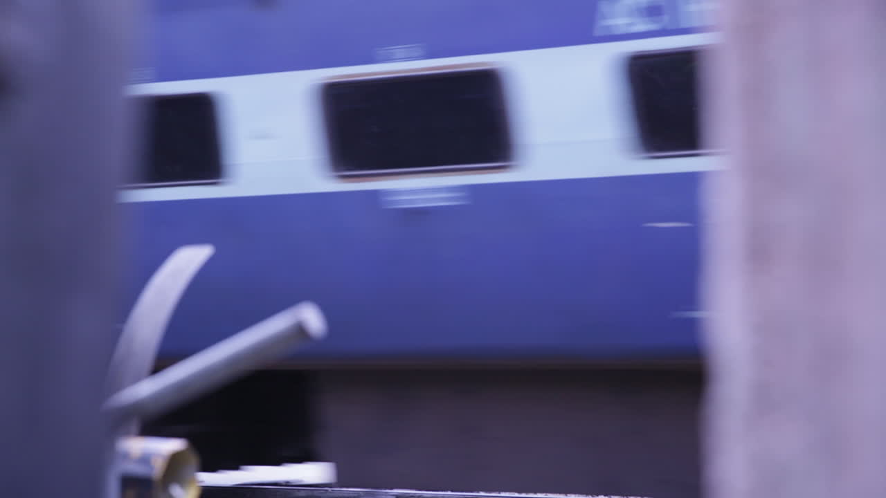 Blue train rushes past a rural railway crossing in Bangalore, Karnataka, India on a sunny day