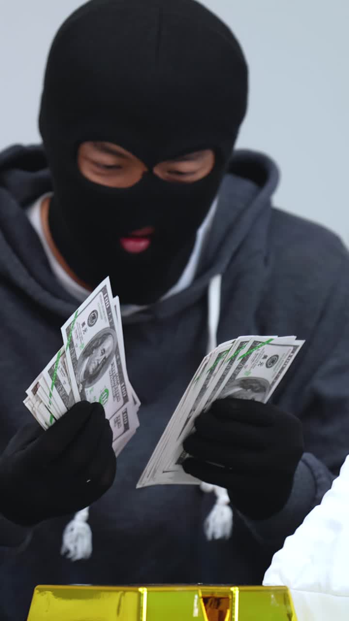 Un criminale con una maschera nera conta banconote da un dollaro sopra lingotti d'oro al chiuso.
