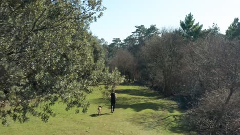 Kaukasische-Frau-Mit-Ihrem-Hund-An-Der-Leine-Joggen-Durch-Bäume-In-Cres,-Kroatien-An-Einem-Sonnigen-Morgen