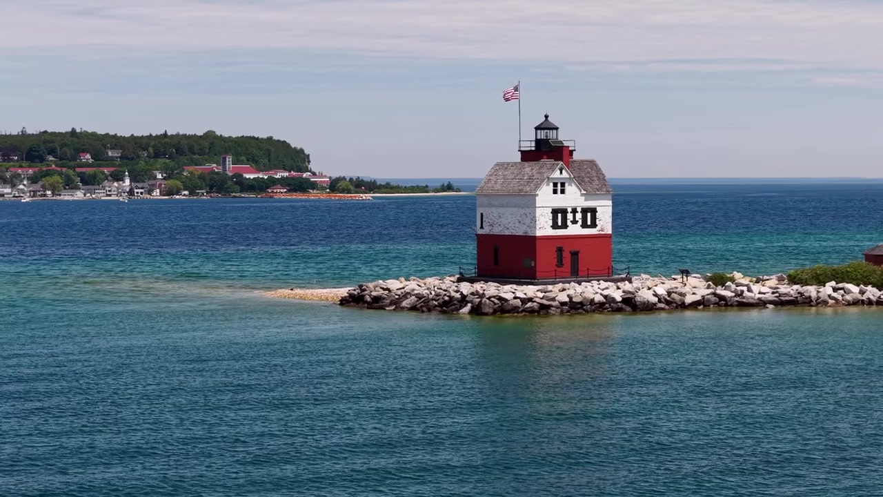 Drone se aproxima do Farol Round Island vermelho e branco, erguido sobre um quebra-mar rochoso perto da Ilha Mackinac, Michigan.