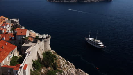 Aerial-View-Of-The-Old-Town-Of-Dubrovnik-With-A-Boat-Sailing-In-The-Adriatic-Sea-In-Croatia---drone-shot