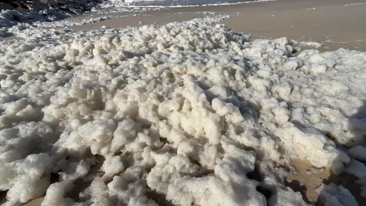 Et stort lag af havskum skabt af stormbølger, der skyller op på stranden