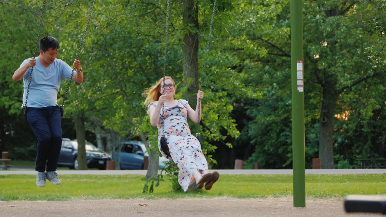 다민족 커플 - 아시아 남자와 임신한 백인 여자가 그네를 타고 행복한 젊은 가족