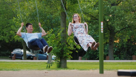 multi-ethnic couple - asian man and pregnant caucasian woman ride on a swing happy young family