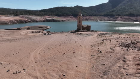 Man-walking-towards-resurfaced-historical-Church-in-Sau-reservoir,-drought