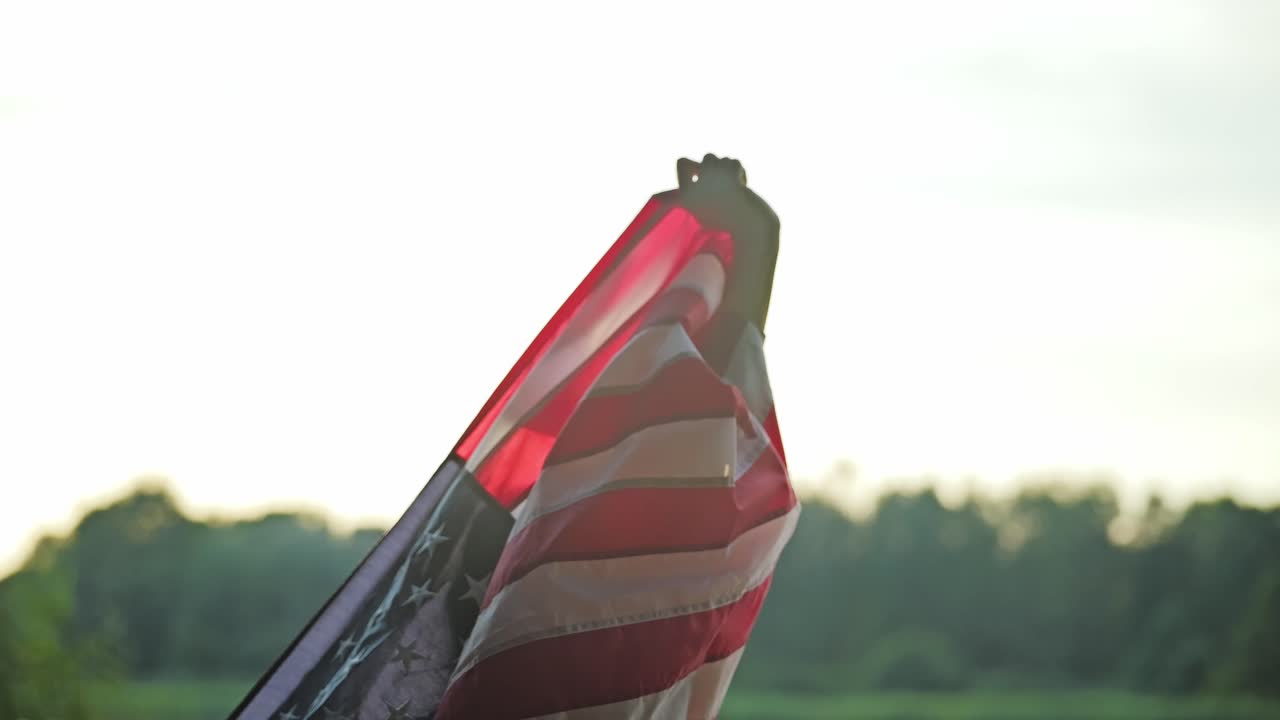 Slowmotion-optagelse af en kvinde, der løfter det amerikanske flag op mod himlen ved en gylden solnedgang.