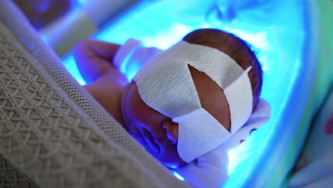 lovely infant having the phototherapy. little newborn lies on a lamp in his crib covered with blanket. top vie close up.