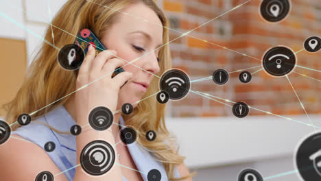 Animation-of-network-of-communication-icons-over-caucasian-woman-talking-on-smartphone-in-office