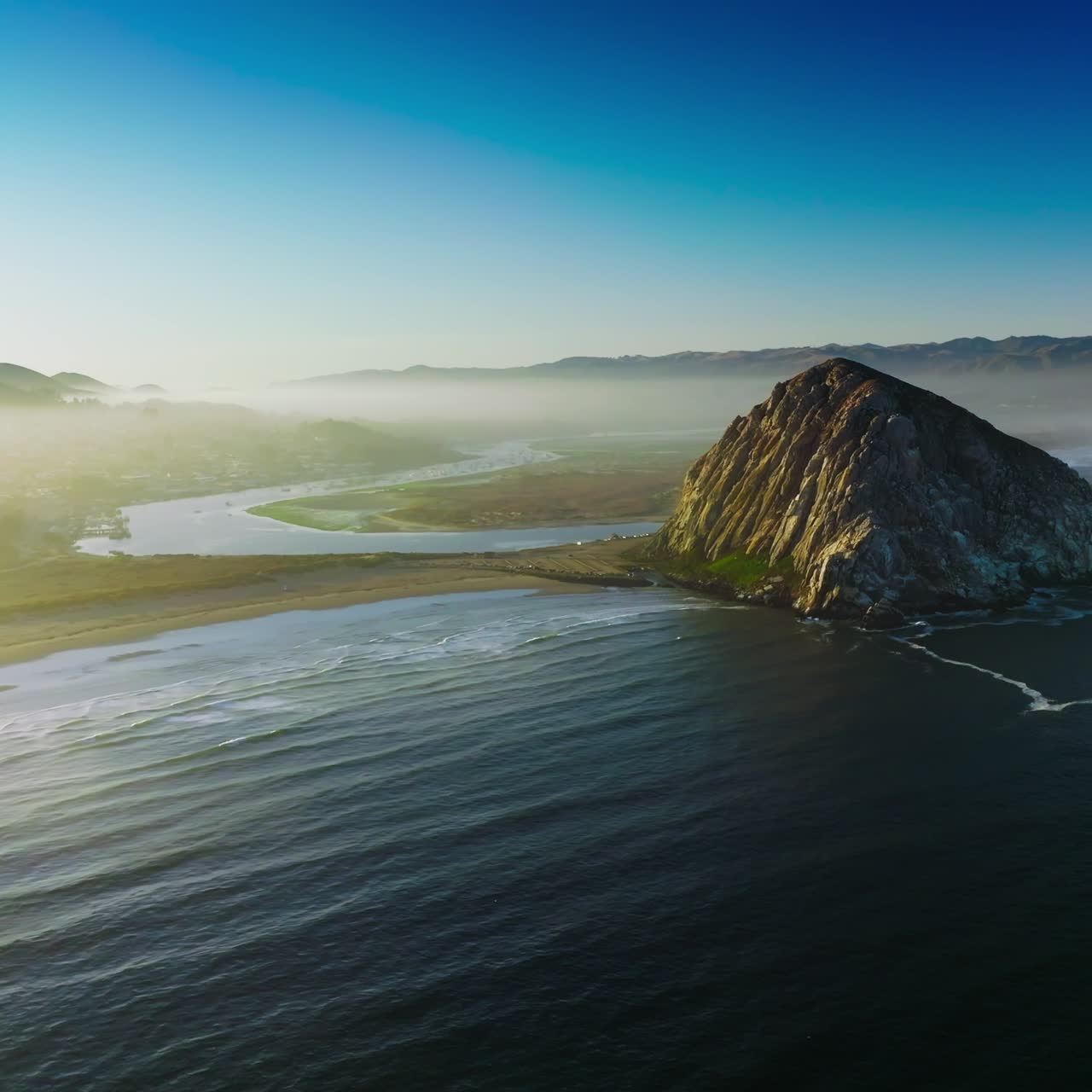 Magical sight of Morro Bay covered with thick fog. Triangle rock at the shore of Central coast of California, USA . Azure sky at backdrop