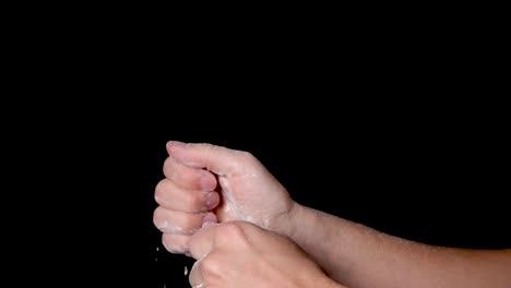 A-person-rubbing-his-hands-and-evenly-distributing-the-chalk-powder,-isolated-on-black-background