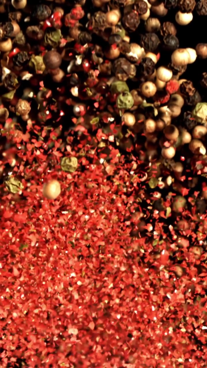 Granos de pimienta variados y hojuelas de chile rojo cayendo en cámara lenta