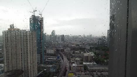 rain drop on window. aerial view. raining outside living room window on rainy season in bangkok thailand. outside window is blurred of raining city building and road and sky.