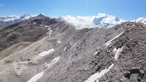 Flight-over-a-hiking-trail-at-Alps-mountains-in-Gornergrat,-Zermatt,-in-Switzerland-with-the-reveal-view-of-a-beautiful-glacier