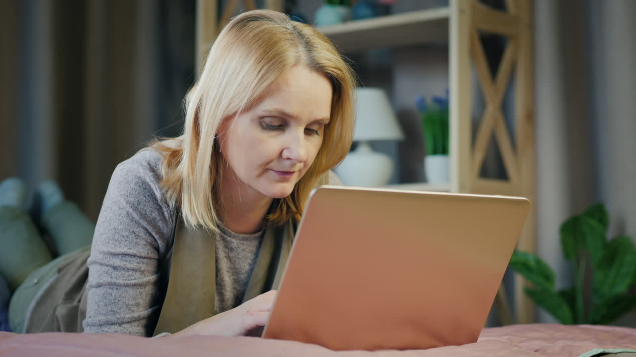 una mujer de mediana edad usa una computadora portátil en su cama 2