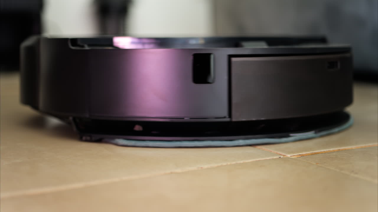 Close up of a black robot vacuum cleaner moving and rotating on the floor tiles
