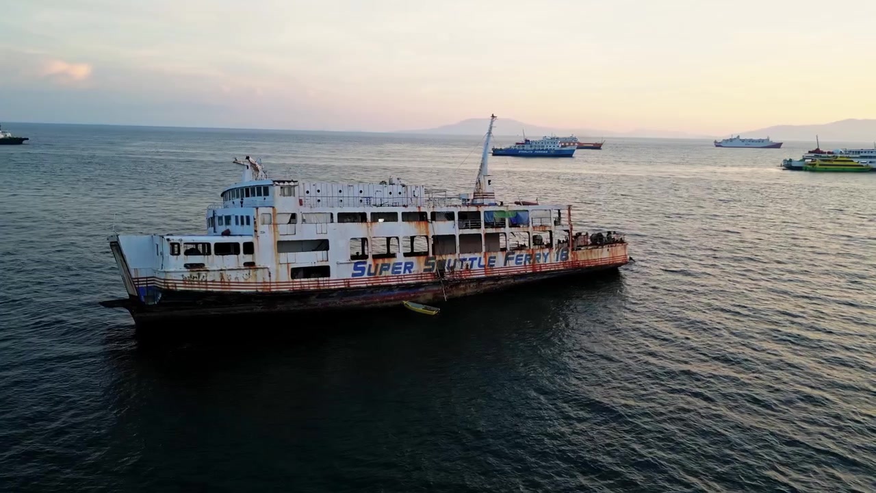 Rivelazione aerea con lenta panoramica di una nave da carico abbandonata che enfatizza l'isolamento nel vasto oceano vicino al porto di Batangas, Batangas City, Filippine