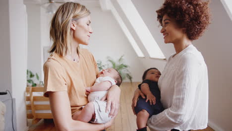 Dos-Madres-Reunidas-Sosteniendo-Bebés-Recién-Nacidos-En-Casa-En-Un-Apartamento-Tipo-Loft