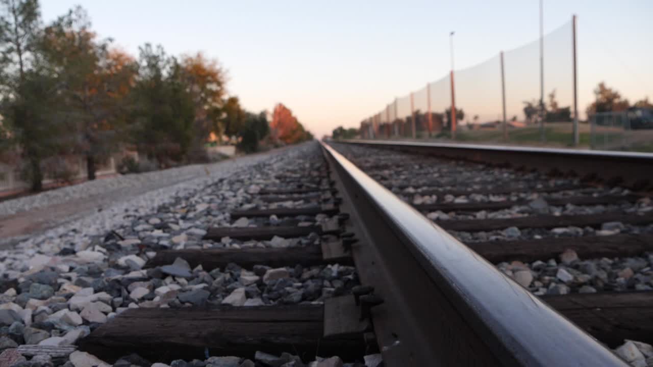 Close side view of empty steel railroad tracks leading to sunset sky