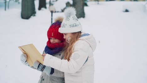 cute kids are holding a large envelope in their hands and reading the address on it in the middle of the street in the winter. chidren are looking for an address of home to give a letter. slow motion. blurred background