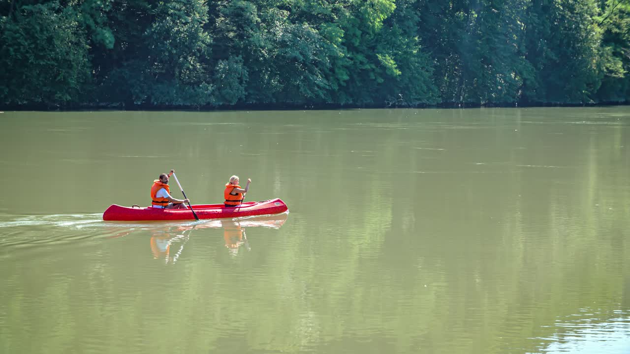 man and woman enjoying canoeing on tranquil river. Forest reflected on the water
