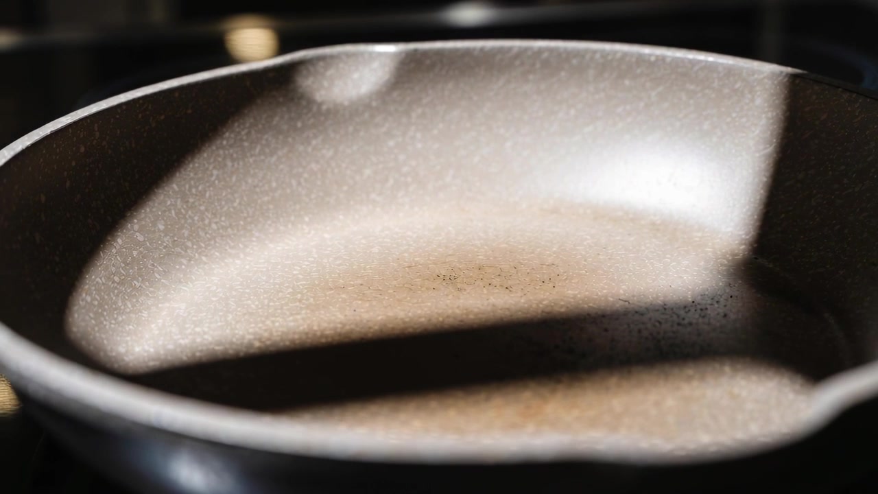 Tightening camera showing speckled nonstick pan on stove, light shifting showing shadow band scuffs