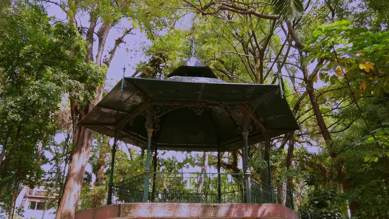 Ampia veduta di un gazebo circondato da fitti alberi tropicali e vegetazione lussureggiante all'interno di un parco pubblico a Cuernavaca, Messico, di giorno.