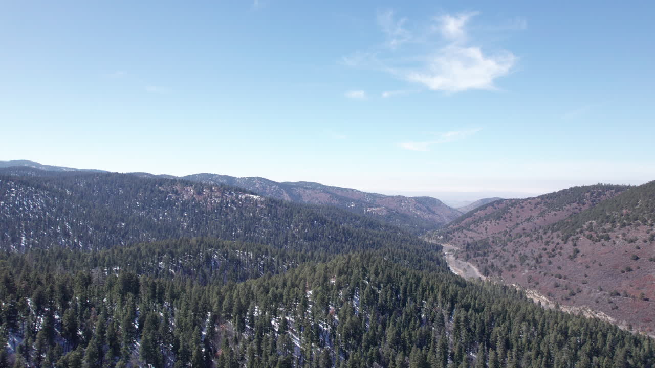 una vista aérea de un valle montañoso de nuevo méxico vuela hacia atrás para revelar una carretera rural.