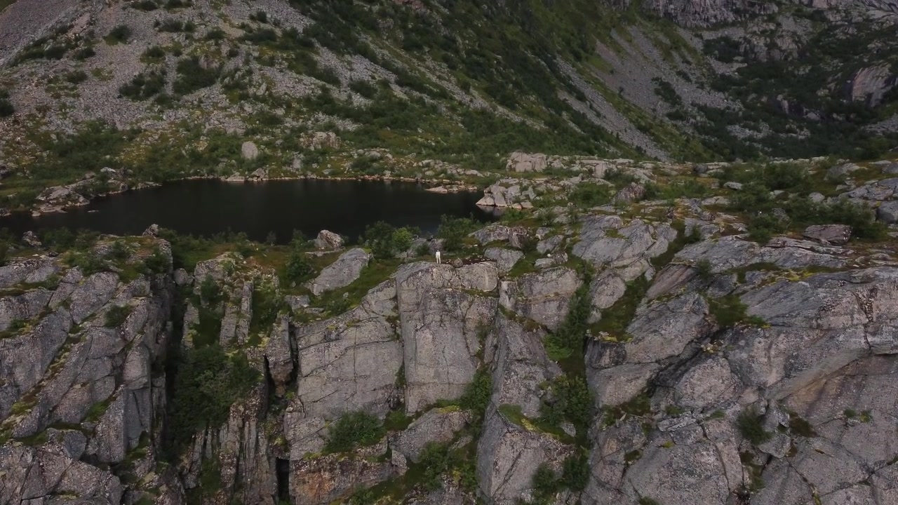 Primo piano su una donna in piedi su una scogliera su una montagna (Festvagtind) in Norvegia con un lago e montagne sullo sfondo
