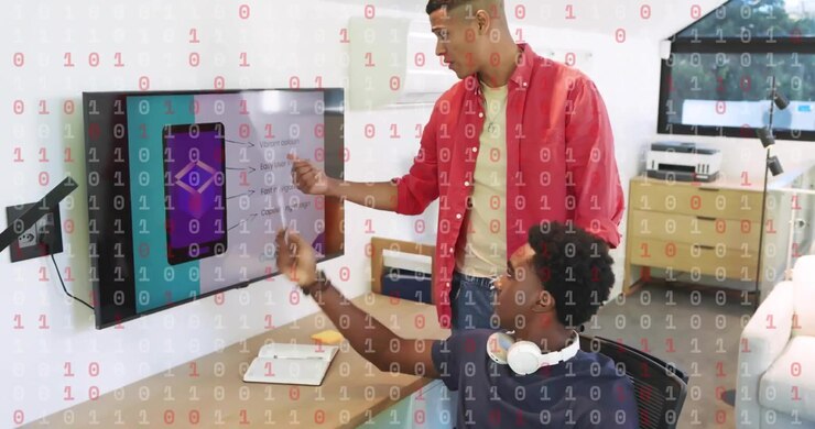 Product manager entering office with documents and guiding seated developer in reviewing app mockup