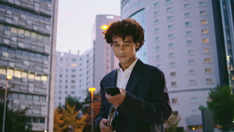 Serious-lawyer-working-phone-at-dusk-street.-Curly-manager-unlocking-smartphone