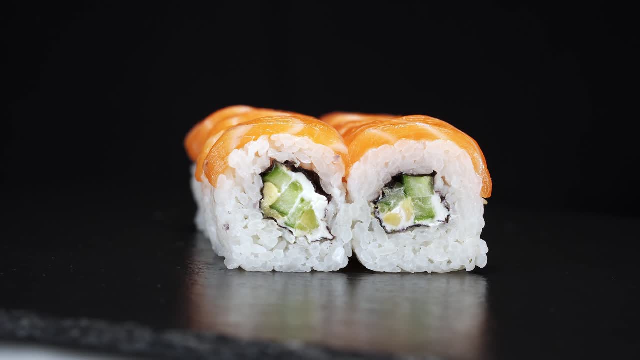 los rollos de sushi giran sobre un fondo negro. grabar en primer plano. queso de filadelfia, pepino y salmón en la comida japonesa.