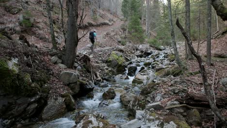 camera from the side in the river stream as the hiker walks past the camera away from the camera up the hil