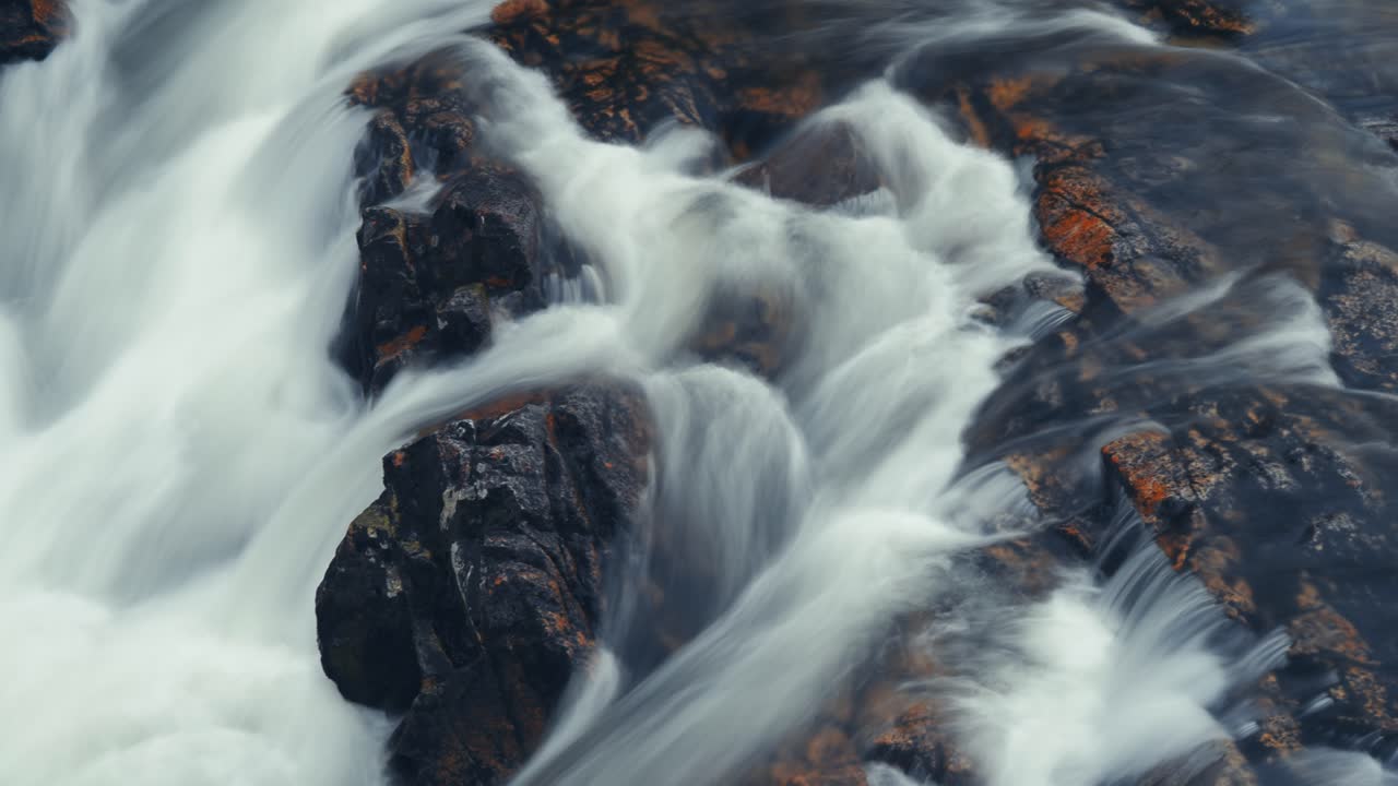 un poderoso flujo de agua blanca sobre las rocas escuras astilladas en el video de larga exposición
