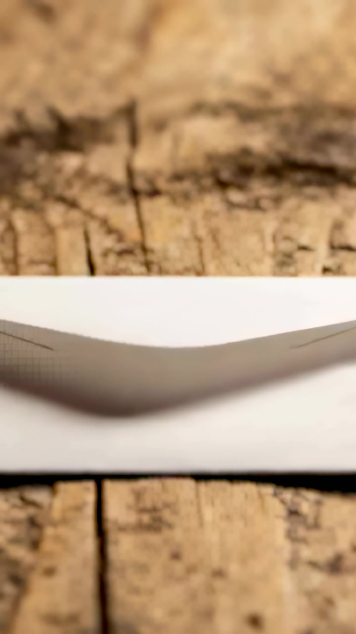 Vertical video: Shifting focus, camera filming white envelope showing V ridge and shadow on plank