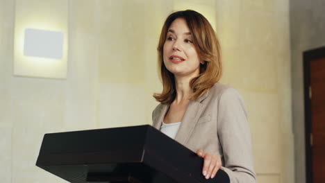 caucasian businesswoman speaker on a podium wearing formal clothes and talking in a conference room