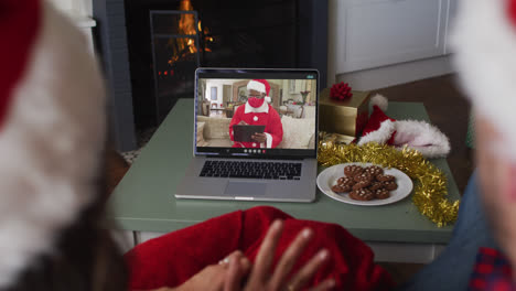 Rückansicht-Eines-Kaukasischen-Paares-Mit-Weihnachtsmützen,-Das-Während-Der-Weihnachtszeit-Einen-Videoanruf-Auf-Dem-Laptop-Führt