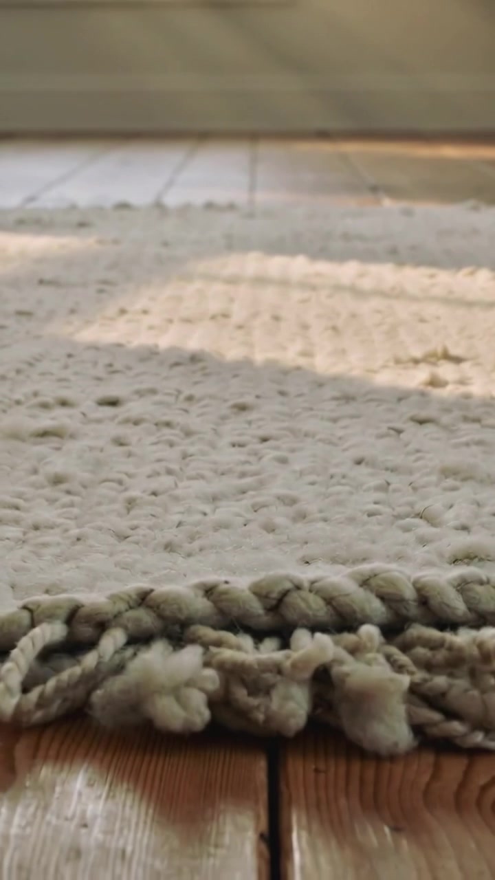 Vertical video: Camera pulling back showing off-white braided rug fringe on floor, sun, base, tufts