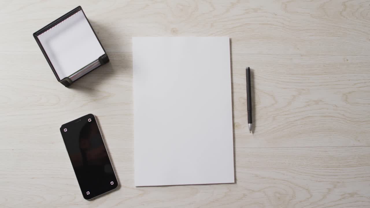 Video of smartphone and white sheet of paper with pen and copy space on wooden background