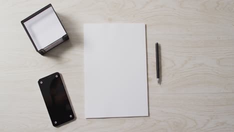 Video-of-smartphone-and-white-sheet-of-paper-with-pen-and-copy-space-on-wooden-background