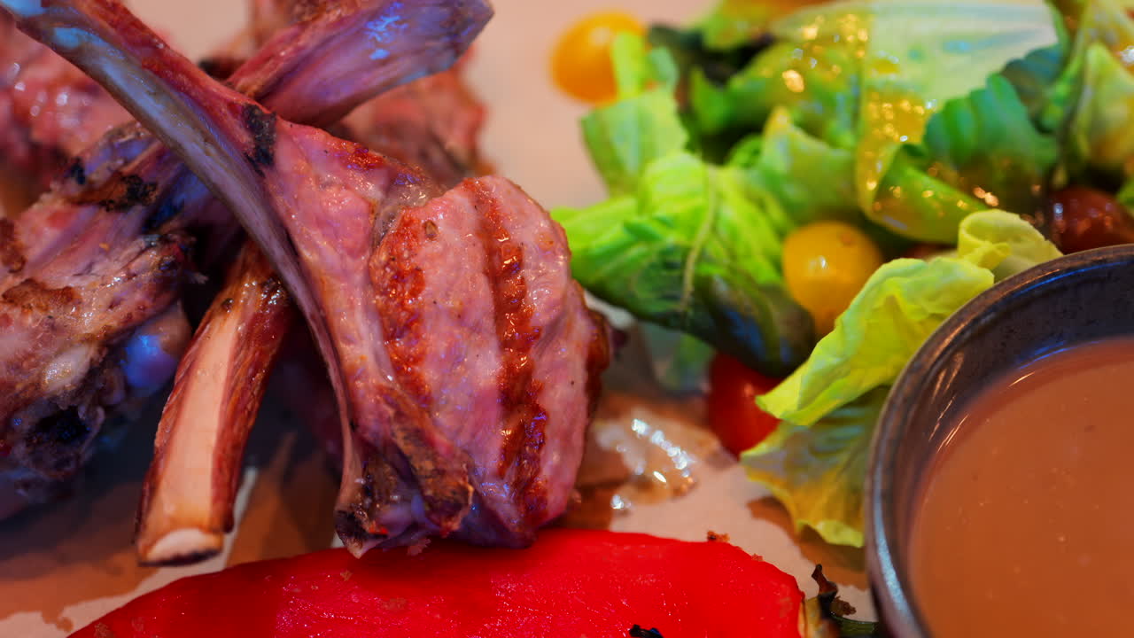 Close up of lamb chops with sauce and a side salad on a plate at a restaurant
