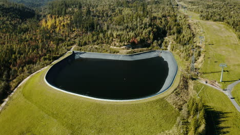 Topshot-wide-aerial-drone-view-of-the-water-dam-in-the-High-Tatras,-surrounded-by-lush-green-summer-trees-and-hills-in-Slovakia,-Europe