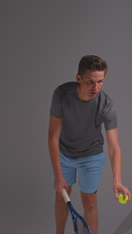 vertical video studio shot of male tennis player serving in match hitting ball with racket against grey background 1