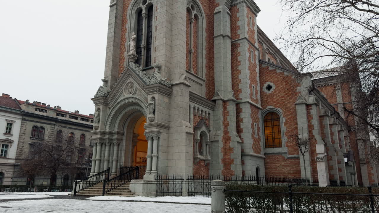 Vista invernale della parrocchia di San Francesco d'Assisi a Budapest, con architettura cattolica storica, facciata in pietra decorata e dintorni innevati in un tranquillo contesto urbano europeo
