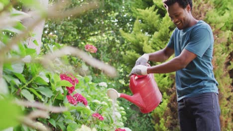 Hombre-Birracial-Feliz-Haciendo-Jardinería,-Regando-Plantas-Con-Regadera