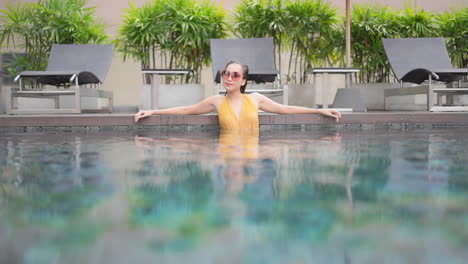 fresh from a swim a strong attractive woman leans along the wall of a resort swimming pool