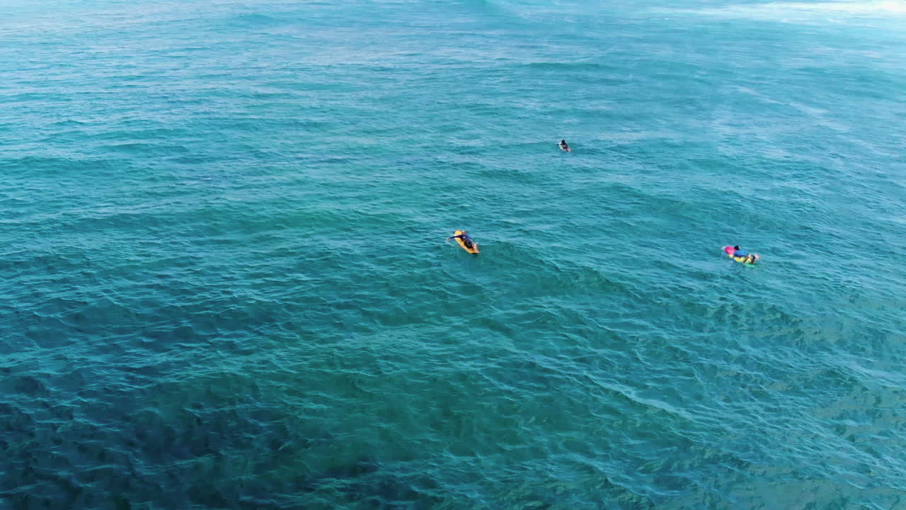 imágenes aéreas de tres surfistas remando hacia las olas en un hermoso océano claro