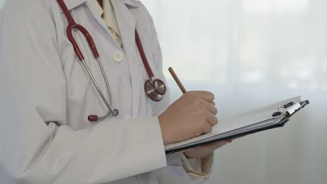 4k 50fps, un médico asiático con una bata blanca se para para tomar nota de la condición del paciente en la sala de exámenes.
